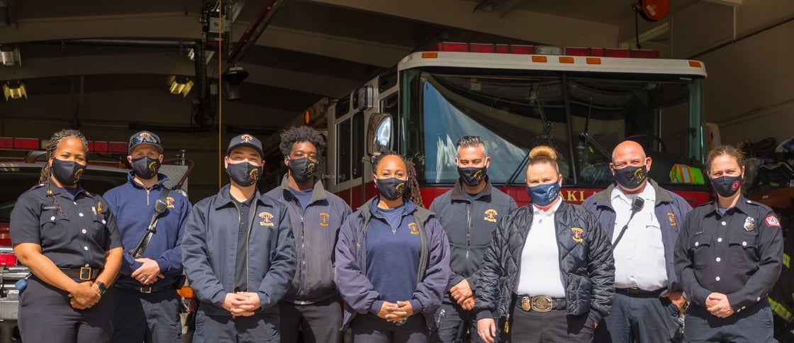 Oakland fire inspectors stand side-by-side in front of fire trucks